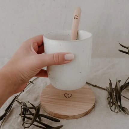 Witte gespikkelde keramische mok met houten lepel en hart-onderzetter in Scandinavische setting